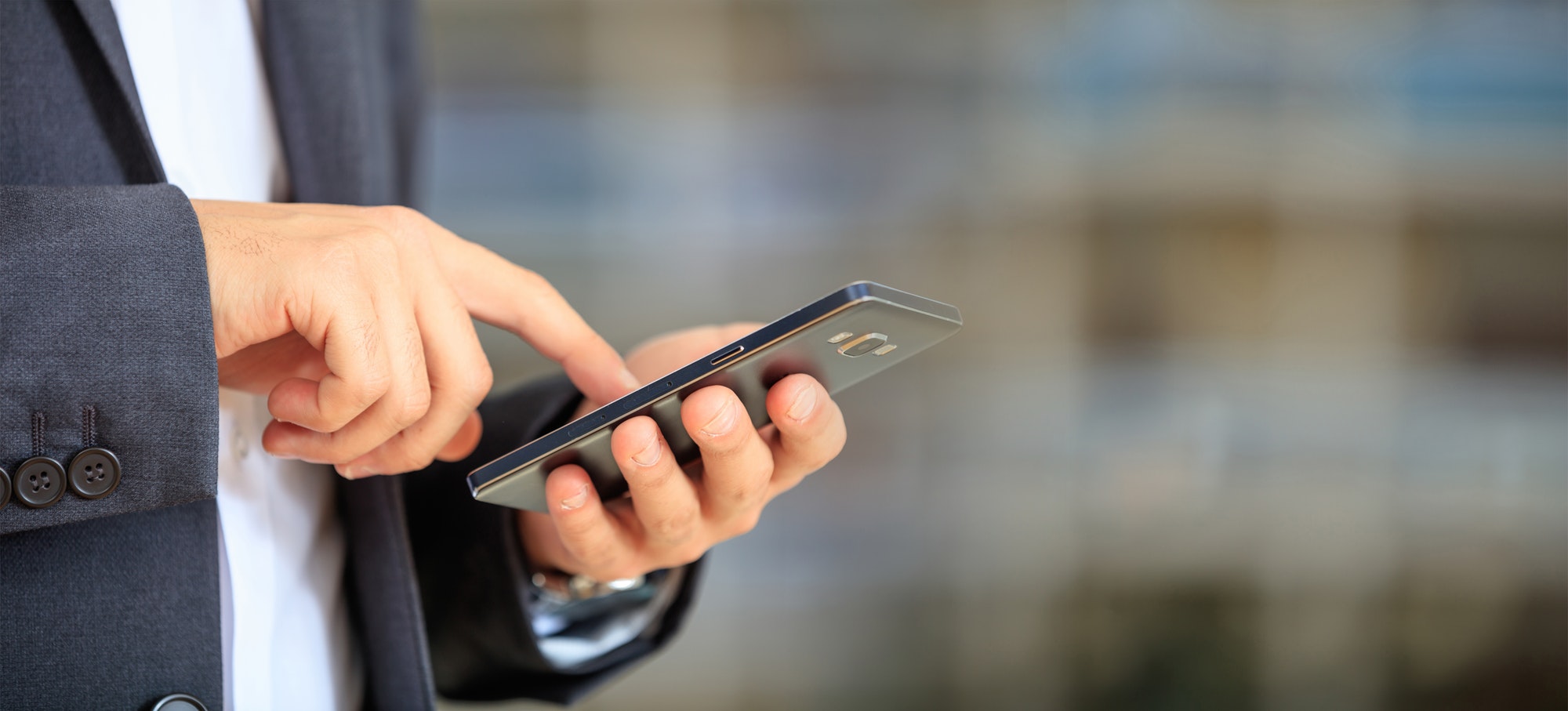Man holding phone. Young businessman in business wear using a mobile, closeup view on smartphone